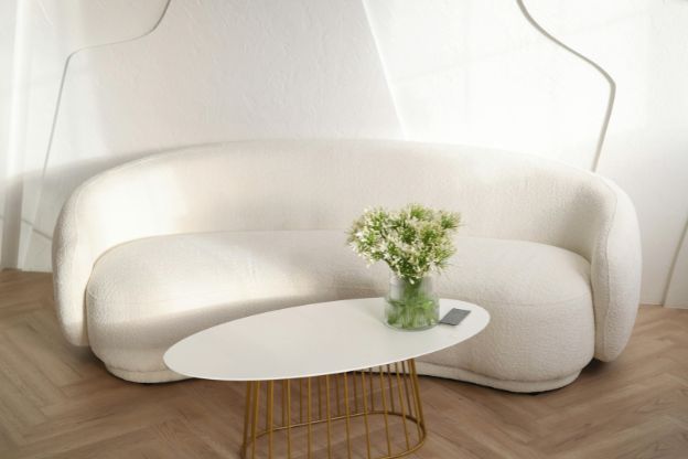 Round white couch with coffee table and flower vase.